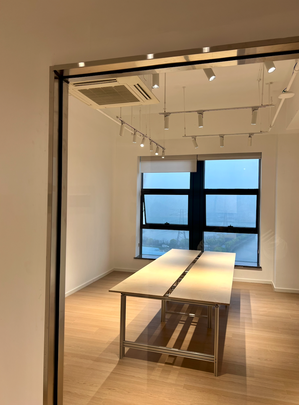 图片展示的是贾维斯联盟·杭州滨江“AI联合战队”场地内的一间空旷房间。房间内有一张长方形的白色桌子,桌面中间有黑色线条装饰,桌子下方有金属支架。房间地面铺有木质地板,墙面为白色。天花板上装有多个白色射灯 addCriterion图片内容